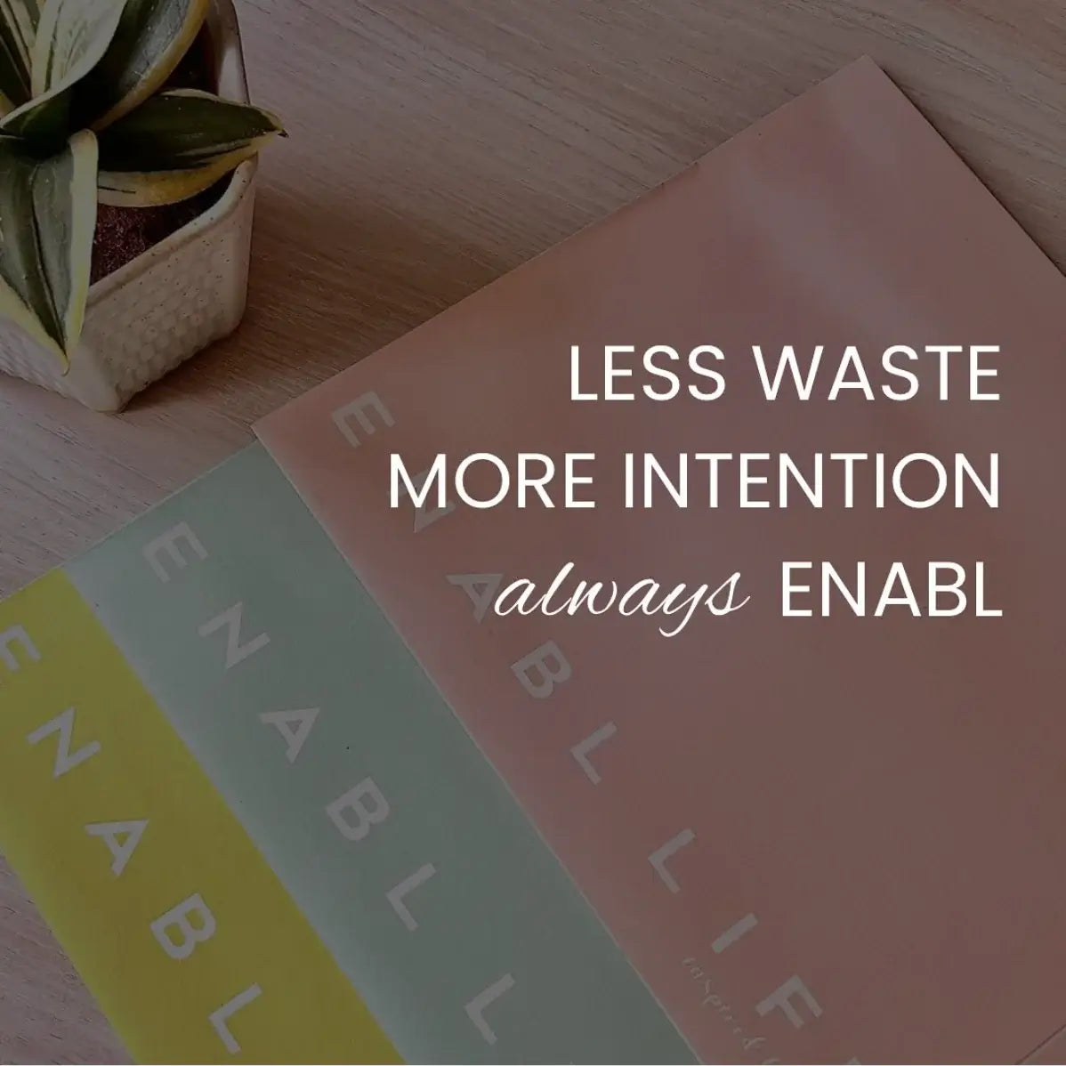 Colorful books with 'LESS WASTE MORE INTENTION always ENABL' text on a wooden surface.